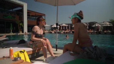 Havuz başında sohbet ederken, mayo giymiş iki güzel kız boş zamanlarının tadını çıkarıyorlar. Yüksek kalite 4k görüntü