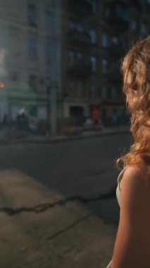 Kıvırcık saçları ve atletik titreşimleriyle genç bir kız bir yaz günü şehirde yürüyor. Yüksek kalite 4k görüntü
