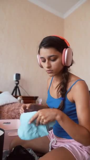 Fiatal Gyönyörű Összecsukja Holmiját Egy Bőröndbe Miközben Zenét Hallgat Fejhallgatóján — Stock videók