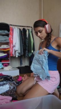 Kız odasında yerde oturuyor, kulaklıklarıyla müzik dinliyor ve elbiselerini katlıyor. Yüksek kalite 4k görüntü