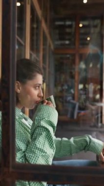 Yazlık kafelerin terasında, güzel bir genç bayan kahve içiyor ve elinde akıllı bir telefon tutuyor. Yüksek kalite 4k görüntü
