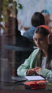 Bir kahve dükkanında, kulaklıklı hoş bir genç bayan dizüstü bilgisayar kullanıyor. Yüksek kalite 4k görüntü