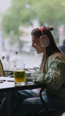 Kulaklıkları yerinde olan genç bir kadın, bir kahve dükkanında dizüstü bilgisayarla iletişim kuruyor. Yüksek kalite 4k görüntü