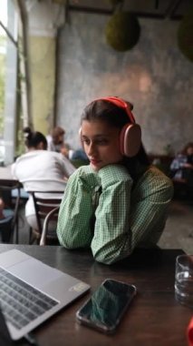 Bir kafede, bir kız dizüstü bilgisayarı üzerinde çalışırken kulaklık kullanıyor. Yüksek kalite 4k görüntü