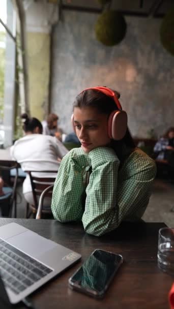 Μια Καφετέρια Ένα Κορίτσι Χρησιμοποιεί Ακουστικά Ενώ Δουλεύει Στο Λάπτοπ — Αρχείο Βίντεο