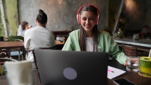 Kawiarni Młoda Kobieta Słuchawkami Rozmawia Przez Laptopa Wysokiej Jakości Materiał — Wideo stockowe