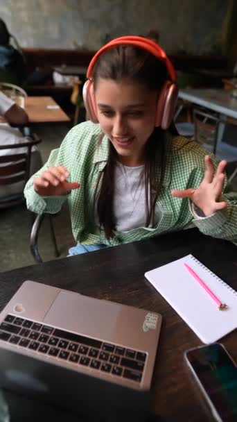 Een Koffieshop Praat Een Jonge Vrouw Met Koptelefoon Haar Laptop — Stockvideo