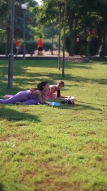 Bir anne ve yetişkin kızı spor yapıyor ve park çimlerinde vücut esnekliği egzersizleri yapıyorlar. Yüksek kalite 4k görüntü