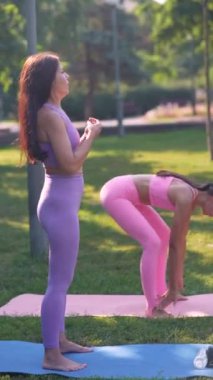 Yetişkin kızıyla birlikte sportif ve çekici bir anne şehir parkında yoga yapıyor. Yüksek kalite 4k görüntü