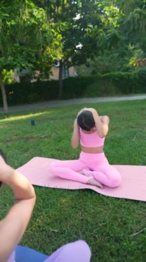 Şehir parkında, sportif ve sevimli bir anne ve yetişkin kızı yoga egzersizleri yapıyorlar. Yüksek kalite 4k görüntü