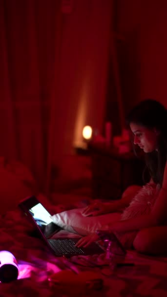 薄暗い部屋でベッドに座って 若い女性が寝室でラップトップに取り組んでいる 高品質の4K映像 — ストック動画
