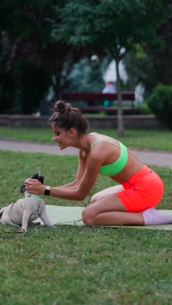 公園では 運動服を着た若い女性が芝生の上の彼女のパグ犬と遊び心のある活動に従事しています 高品質の4K映像 — ストック動画