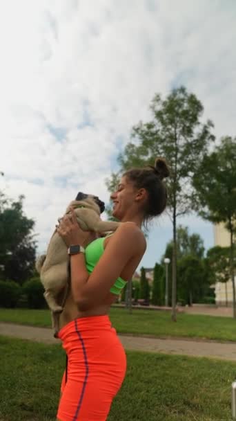 在一个夏季的公园里 一名年轻的女运动员抱着一只哈巴狗进行日常的体育运动 高质量的4K镜头 — 图库视频影像