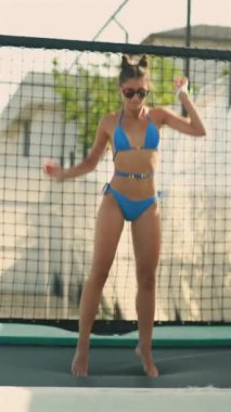 Plaj, bikinili güzel bir kızın trambolinde zıplamasıyla eğlenceli bir yer haline geliyor. Yüksek kalite 4k görüntü
