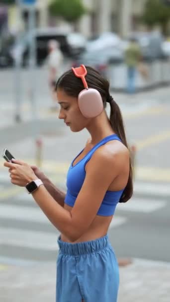 彼女のルートを走っていると 運動服とヘッドフォンの女の子が彼女のスマートフォンを見ます 高品質の4K映像 — ストック動画