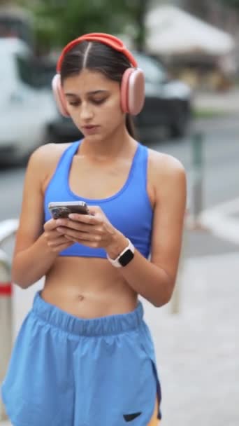 Zaangażowana Bieganie Ładna Dziewczyna Sportowym Stroju Słuchawkach Sprawdza Swojego Smartfona — Wideo stockowe