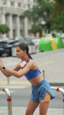 Koşuya çıkan atletik giysili güzel bir kız şehir sokaklarında ısınma hareketleri yapıyor. Yüksek kalite 4k görüntü