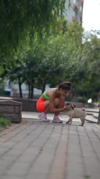 ゆったりとした散歩に従事し かわいい女の子が街の通りを通り抜ける彼女のパグ犬を伴う 高品質の4K映像 — ストック動画