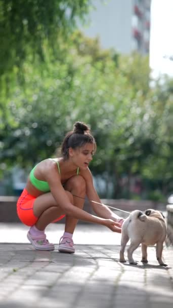Şehir Sahnesinde Spor Giysili Bir Kız Pug Köpeğiyle Oynarken Eğleniyor — Stok video