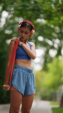 Koşusundan önce, spor elbiseli genç bir kız ısınma rutinine bir direniş bandı dahil ediyor. Yüksek kalite 4k görüntü