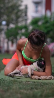 Parktaki sabah eğitiminin ortasında, sportif bir kız pug köpeğiyle güzel vakit geçiriyor. Yüksek kalite 4k görüntü