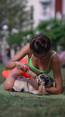 Parkta sabah antrenmanına çıkan spor kıyafetli bir kız pug köpeğiyle eğlenceli bir seans yapıyor. Yüksek kalite 4k görüntü