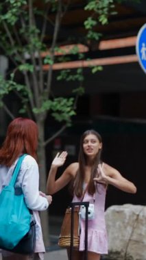 Çantalı iki genç ve güzel arkadaş ve bir bavul şehrin sokaklarında konuşuyorlar. Yüksek kalite 4k görüntü