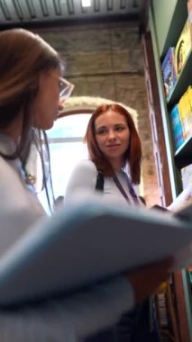 Kitapçıda, kitapların arasında iki güzel kız sohbet ediyor. Yüksek kalite 4k görüntü