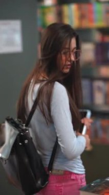 Kitapçıların ortasındaki davetkar atmosferde genç ve enerjik bir bayan kitapların arasında geziniyor. Yüksek kalite 4k görüntü