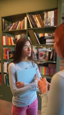 Etrafı kitaplarla çevrili, elinde kitap olan iki sevimli arkadaş kütüphanedeler. Yüksek kalite 4k görüntü