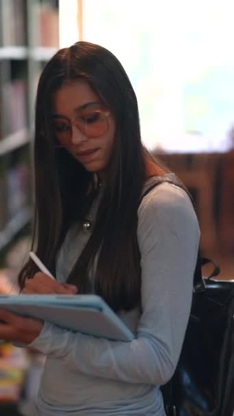 在书店挑选书的过程中 一位年轻貌美的女士正在书架上悠闲地散步 高质量的4K镜头 — 图库视频影像
