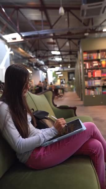 美しく若々しい少女が図書館のソファーに座っている 高品質の4K映像 — ストック動画