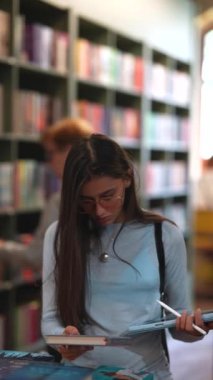 Etrafı kitaplarla çevrili, çarpıcı genç bir kadın kitapçıda boş boş dolaşıyor. Yüksek kalite 4k görüntü