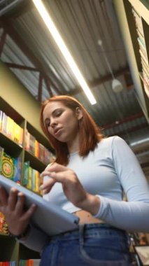 Elinde tabletle genç ve güzel bir kadın kütüphanede konuşuyor. Yüksek kalite 4k görüntü