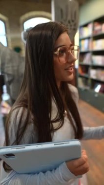 Elinde tablet olan genç ve çekici bir bayan kitapçıyla ilgili bilgi paylaşıyor. Yüksek kalite 4k görüntü