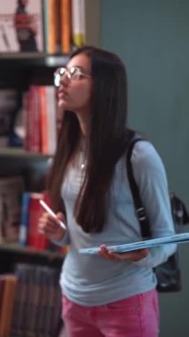 Kitapçıda, neşeli genç bir kız kitaplıkların arasında rahatça yürüyor. Yüksek kalite 4k görüntü