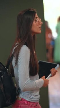 Kitapçıdaki kitaplıklar arasında, hayat dolu genç bir bayan sakin bir yürüyüş yapıyor. Yüksek kalite 4k görüntü