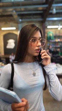 Kütüphane sessizliğinin ortasında, çekici genç bir bayan kitaplıkların arasında bir telefon görüşmesi yapıyor. Yüksek kalite 4k görüntü