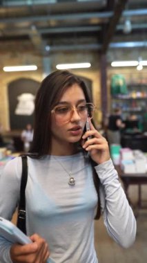 Kütüphane sessizliğinin ortasında, çekici genç bir bayan kitaplıkların arasında bir telefon görüşmesi yapıyor. Yüksek kalite 4k görüntü