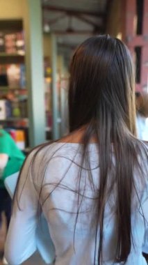 Güzel ve genç bir kız elinde bir tabletle kitaplığın yanında duruyor. Yüksek kalite 4k görüntü