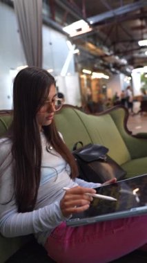 Kitaplarla çevrili çekici genç bir bayan kütüphanedeki bir kanepede görülüyor. Yüksek kalite 4k görüntü