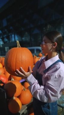 Tedarikçi olarak çalışan genç bir kadın elinde büyük turuncu bir balkabağı ile markette satarken görülüyor. Yüksek kalite 4k görüntü