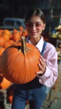 Pazar yerinin ortasında, genç bir bayan satıcı gururla büyük bir portakal kabağı satar. Yüksek kalite 4k görüntü