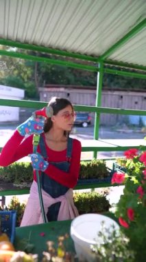 Markette, eldivenli genç bir bayan satıcı sattığı çiçeklerin üzerine su serpiyor. Yüksek kalite 4k görüntü