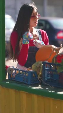 Çiftçi olarak çalışan genç bir kadın, pazarda satılan büyük turuncu bir balkabağı sunarken görülüyor. Yüksek kalite 4k görüntü