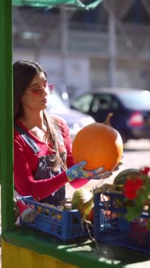 Pazar sahnesinin ortasında, güzel bir kadın satıcı kurbanlarının bir parçası olan balkabaklarını sergiliyor. Yüksek kalite 4k görüntü