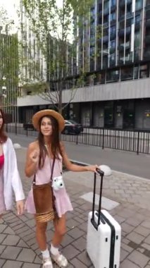 İki enerjik genç bayan ellerinde bir bavul ve eşyayla şehir sokaklarında yürüyorlar. Yüksek kalite 4k görüntü