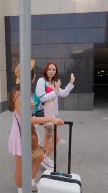 Enerjik genç kızlar, bir bavul ve eşyalarıyla birlikte şehir sokaklarında sakin bir şekilde geziniyorlar. Yüksek kalite 4k görüntü