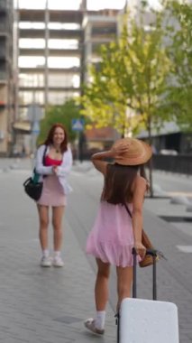 Çantalı iki genç ve güzel arkadaş ve bir bavul şehrin sokaklarında konuşuyorlar. Yüksek kalite 4k görüntü