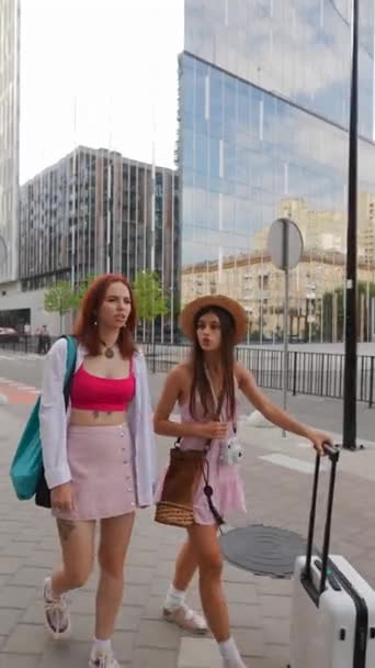 2人の魅力的な若い女性は 街の通りでバッグとスーツケースを運んでいる間 お互いに話し合っているのを見ています 高品質の4K映像 — ストック動画